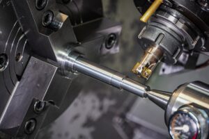 A person in safety glasses carefully aligns a metal workpiece in a CNC milling machine using a dial indicator.