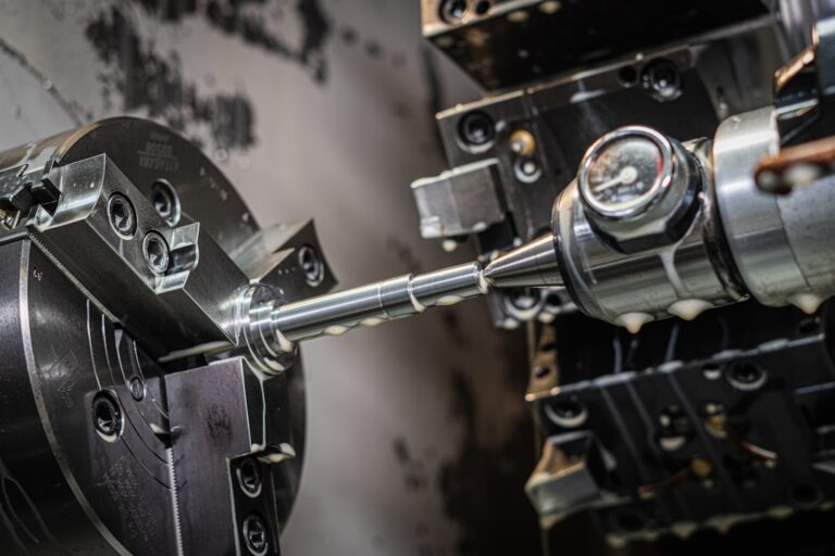 A technician operates a 5-axis CNC machine, adjusting settings on a digital interface next to machined metal components.