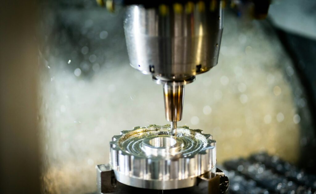 Operator reviews a 3D CAD model beside a CNC machine with cutting tools and metal stock.